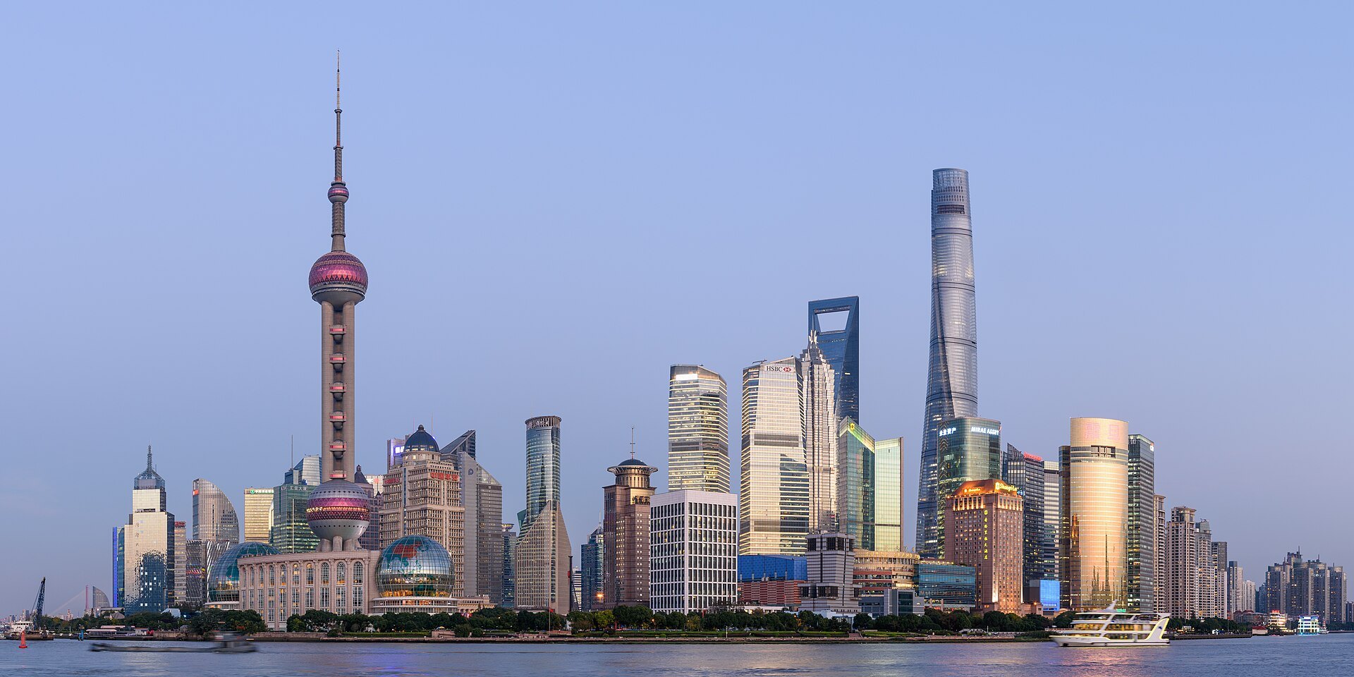 The Pudong skyline across the Huangpu river in daylight — the Oriental Pearl tower and the cluster of supertall towers behind it, with the water in the foreground