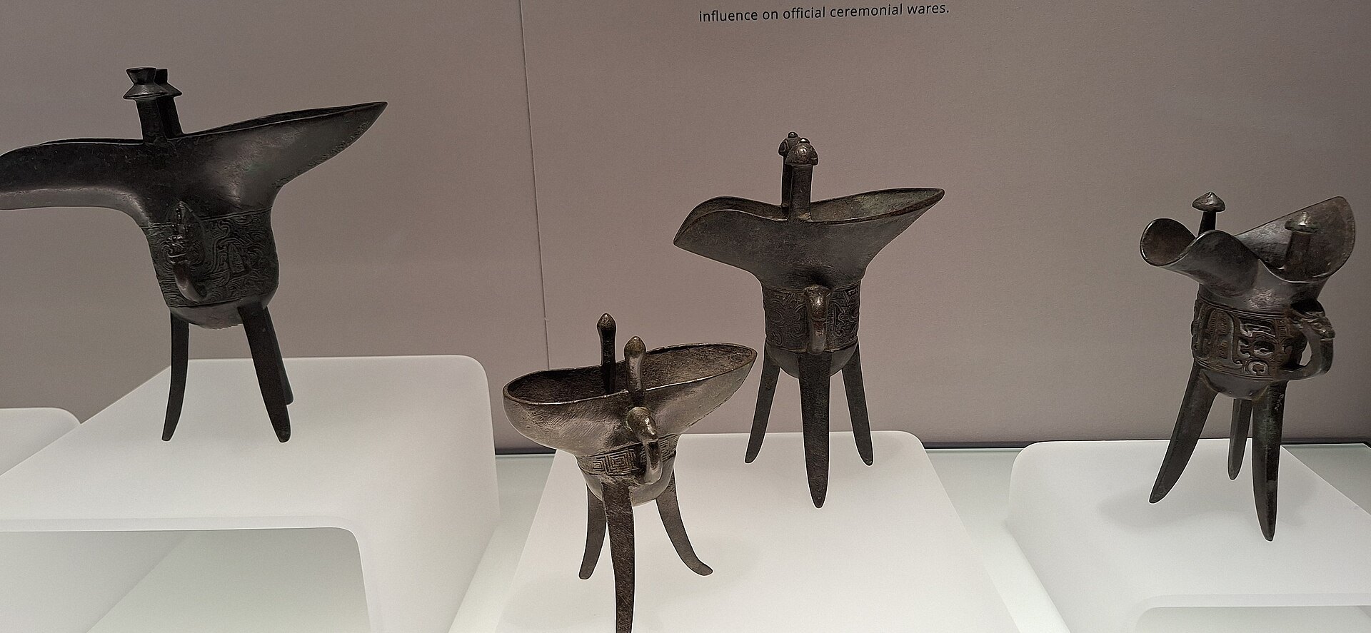 Three-legged bronze vessels in a lit museum case