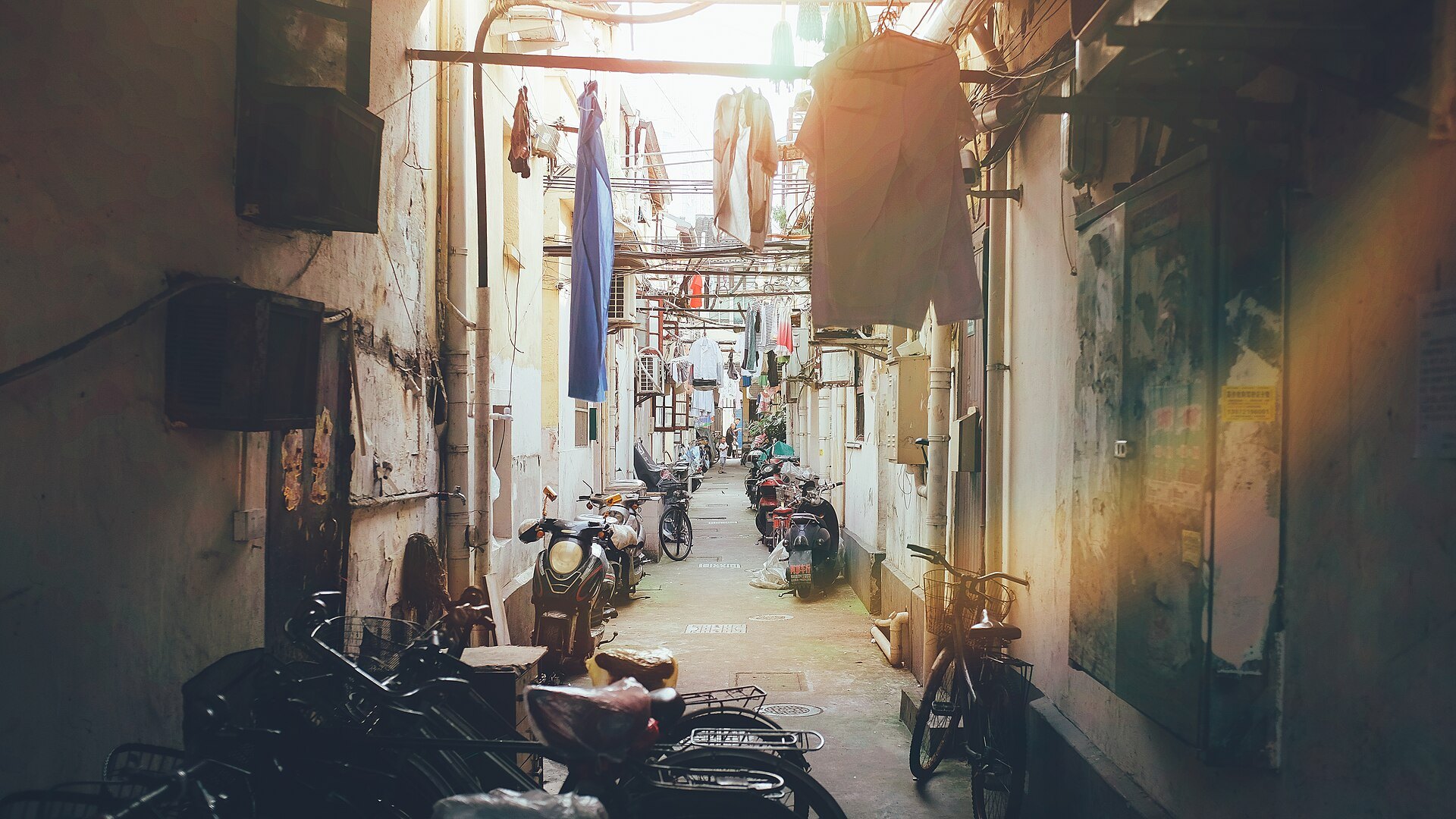 A lane-house alley with motorbikes parked along it in warm afternoon light