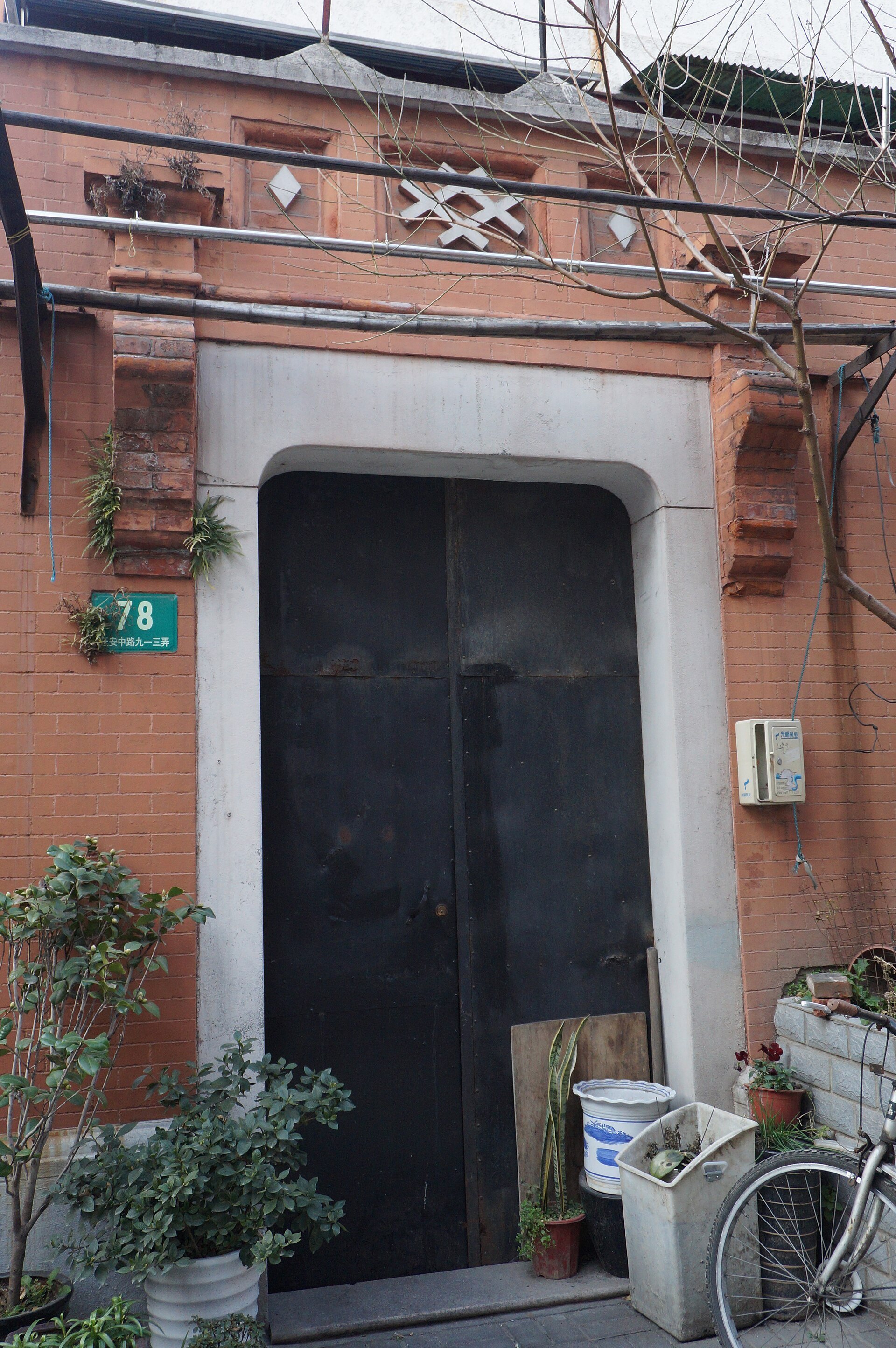 A shikumen stone gateway set into a red brick wall, with plants beside the door